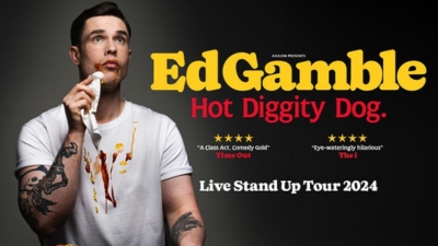 A close up of comedian Ed Gamble messily eating a hot dog. 