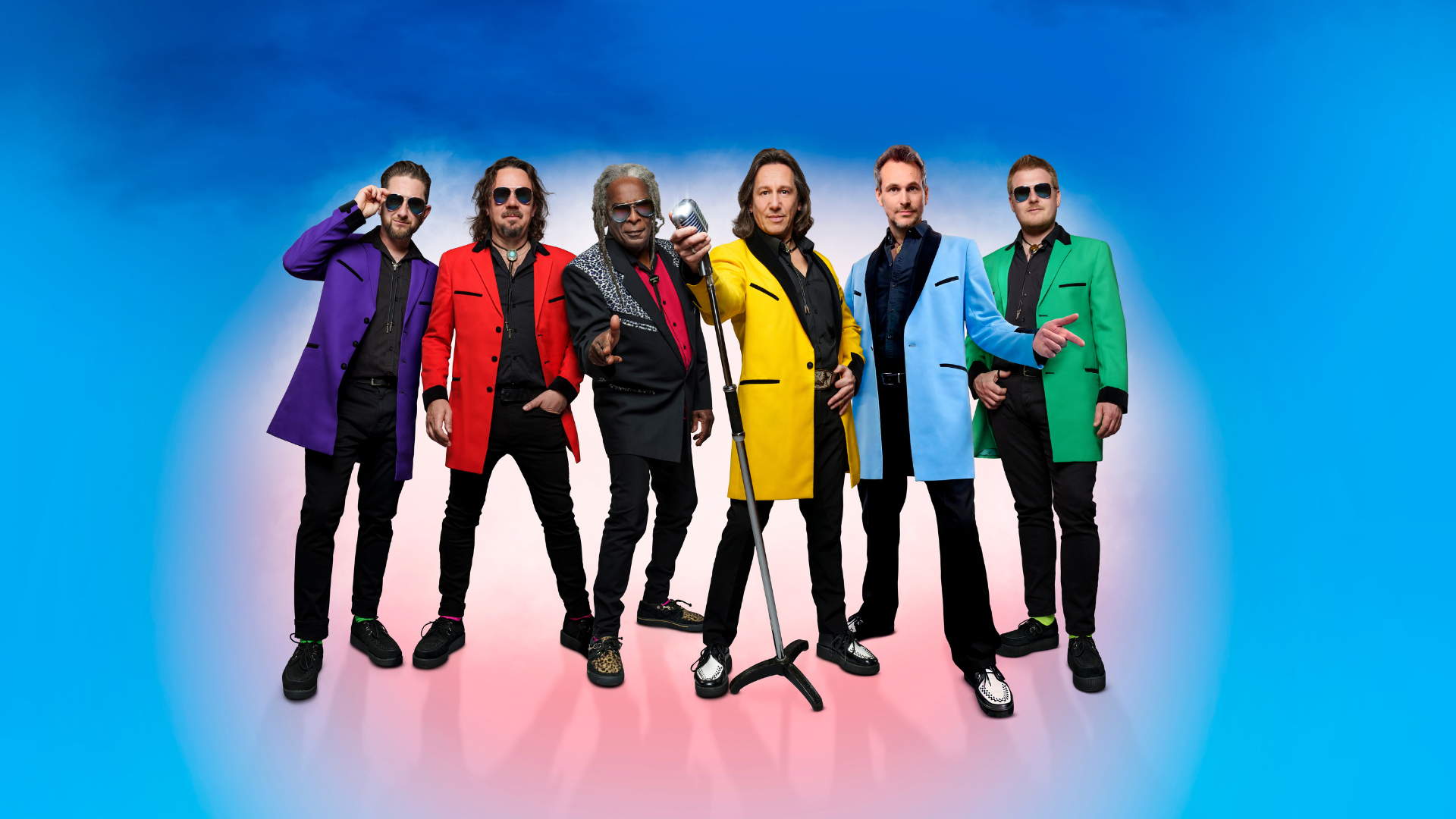 6 Showaddywaddy members stood in a line looking cool. 4 wearing sunglasses and all wearing blacktrouses and bright coats or shirts.