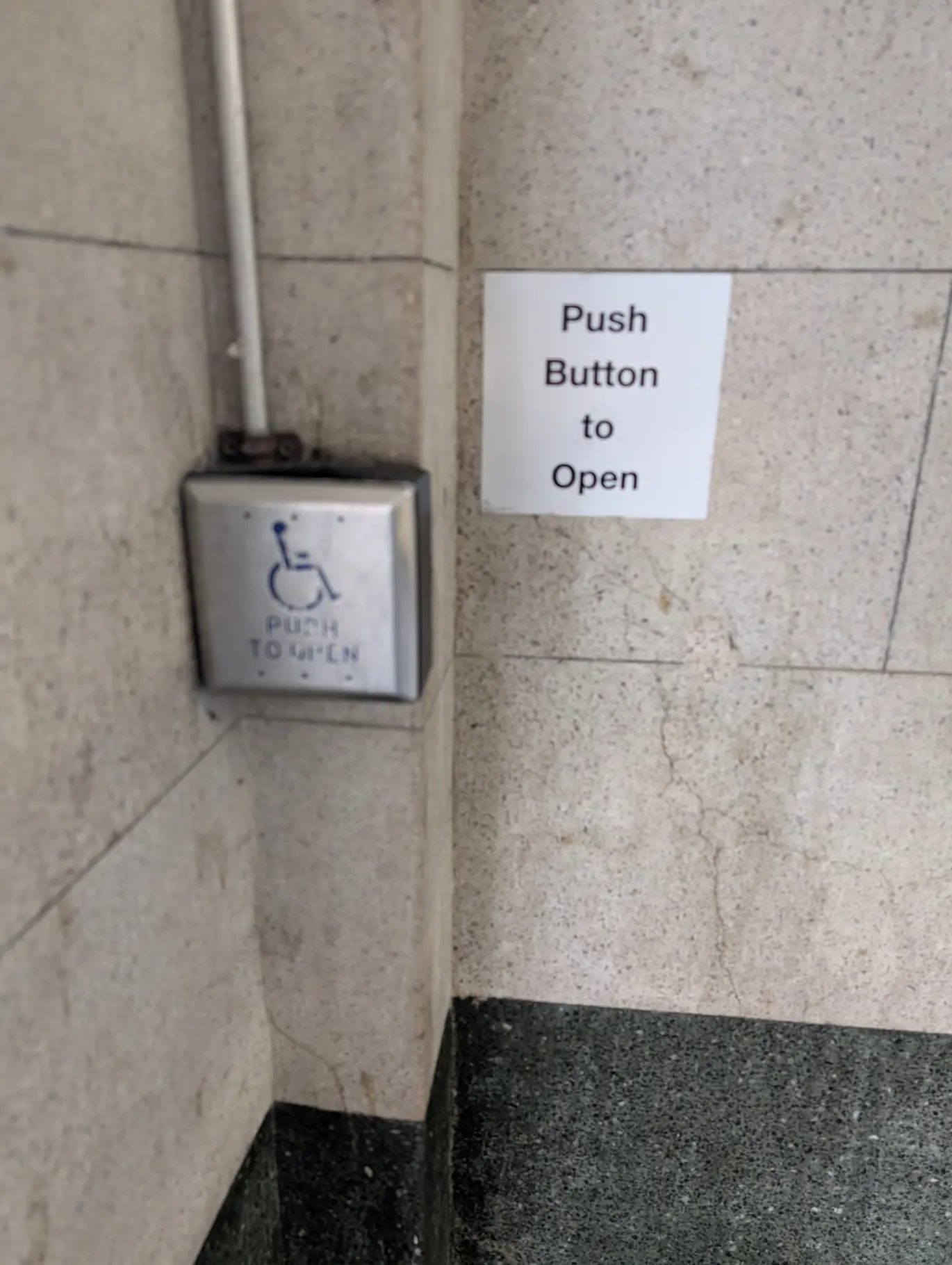 Silver push button to open accessible doors. The button is large and silver,