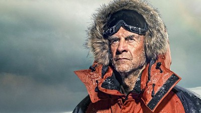 Ranulph Fiennes stands in a hooded coat against a cloudy backdrop. 