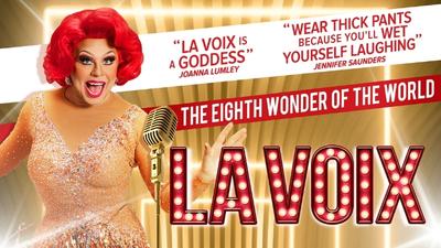 La Voix in a gold dress against a gold, red and white backdrop. 