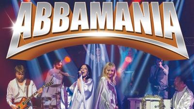 The cast of Abbamania perform on stage with the text 'Abbamania' above them. 