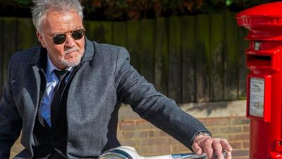 Singer Paul Young rests on a motorbike next to a red post box. 