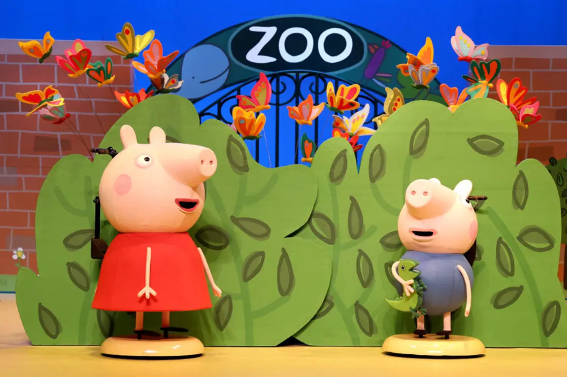 Peppa Pig and Georger talk in front of the entrance to the zoo. 