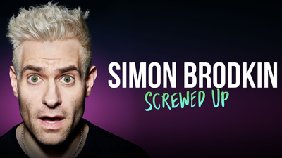 Simon Brodkin with bright blonde hair stares into the camera looking shocked with wide eyes and mouth open.