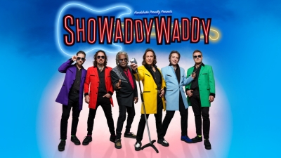 The band members of Showaddywaddy wear colourful blazers as they stand against a bright blue background. 