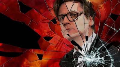 A close up of comedian Ed Byrne staring to the distance against a shattered glass background