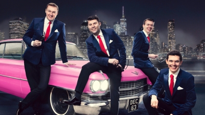 Four men in suits sitting on a pink car.  A city nightscape in the background