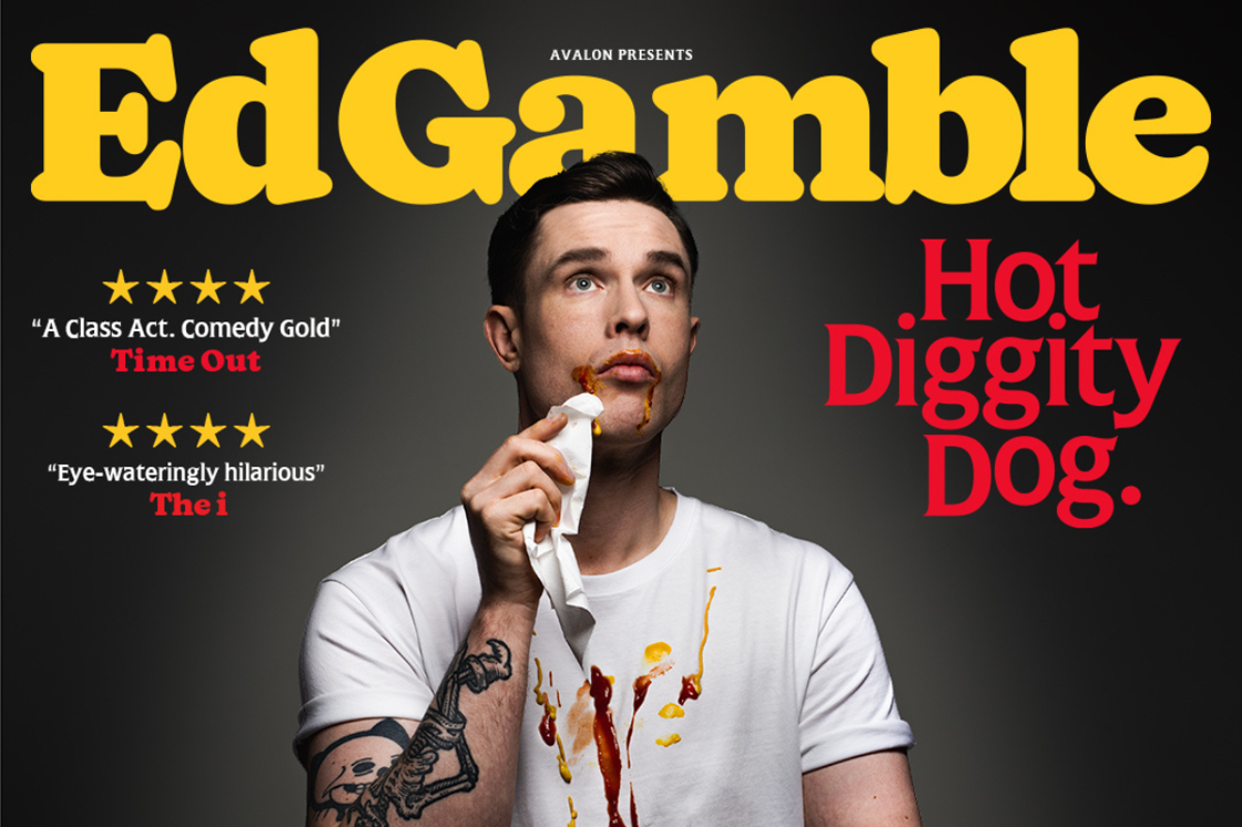 Comedian Ed Gamble with ketchup and mustard on his face and t-shirt, wipes his mouth with a napkin.