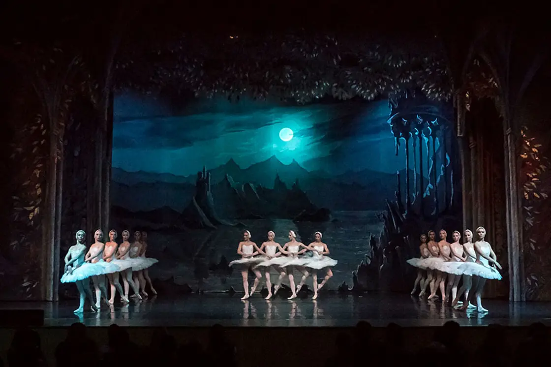 Ballet dancers perform on stage with a backdrop of a moody night sky.