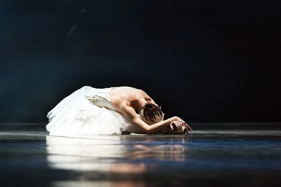 A solo ballet dancer lays on the stage.