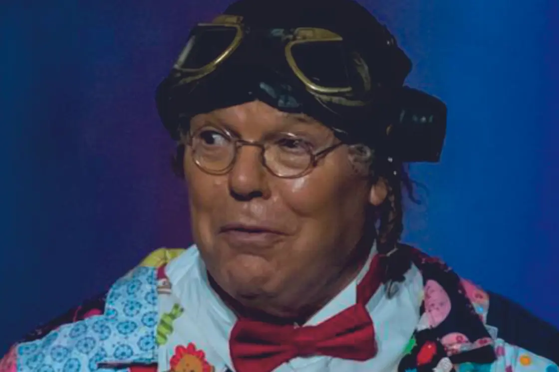 Comedian Roy Chubby Brown stands against a deep purple background.
