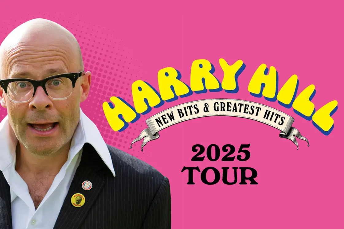 Comedian Harry Hill smiles in front of a hot pink background.